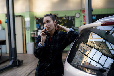 Female mechanic looking away talking on smart phone at repair shop