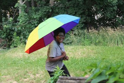 Woman laughing while holding umbrella on field at park