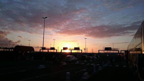 Cars on road against cloudy sky at sunset