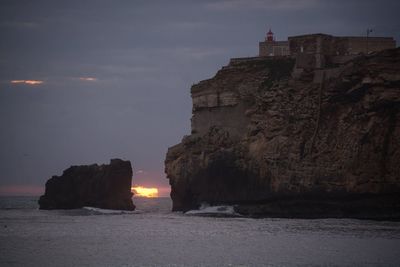 Rock formations by sea against sky at sunset