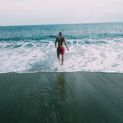 Rear view of shirtless man jumping on beach