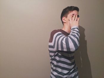 Man covering face while standing against wall