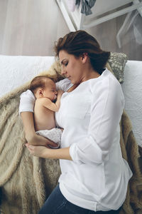 High angle view of mother breastfeeding daughter on bed at home