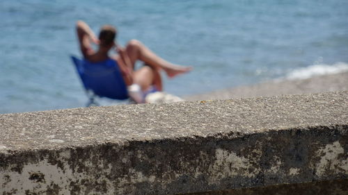 Young woman relaxing on retaining wall by sea