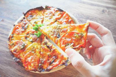 Close-up of hand holding pizza on table