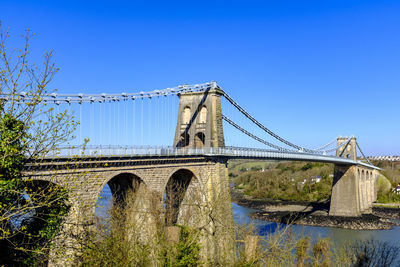 Low angle view of bridge over river against clear blue sky