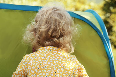 Little girl with blonde curly hair peeking into tent.