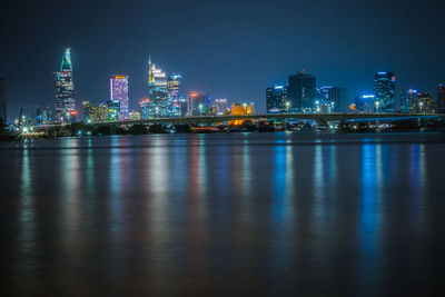 Illuminated cityscape by river against clear sky at night