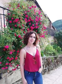 Portrait of beautiful young woman standing by pink flowering plants