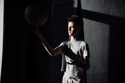 Young man looking away while standing against wall at home