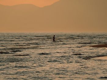 Silhouette person in sea against sky during sunset