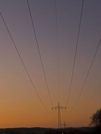 Low angle view of power lines against sky at sunset