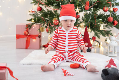 Full length of cute baby girl sitting on bed against christmas decoration