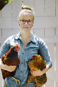 Portrait of woman holding chickens against wooden door