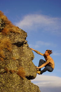 Low angle view of man standing on rock against sky