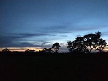 Silhouette trees on landscape against sky at sunset