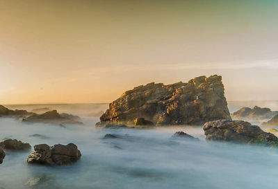 Rocks in sea against sky during sunset