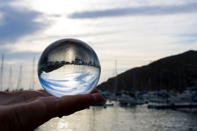 Close-up of hand holding crystal ball against sky