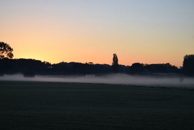 Silhouette trees on field against sky during sunset