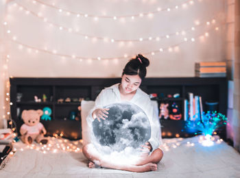 Digital composite image of young woman sitting with moon on bed