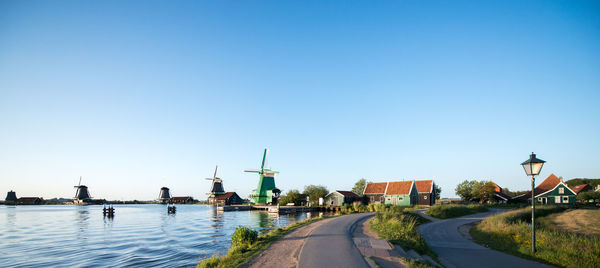 Empty roads and traditional windmills by canal against clear sky