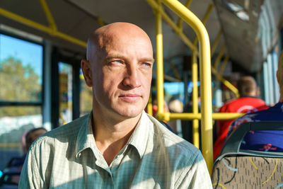 Bald caucasian man rides in public transport while sitting by the window