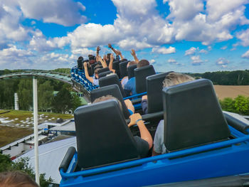 Rear view of people sitting in rollercoaster against cloudy sky