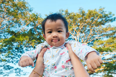 Cropped hands of mother holding son against trees