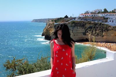 Woman standing by retaining wall against sea against clear sky