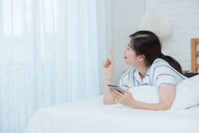 Young woman using mobile phone while sitting on bed