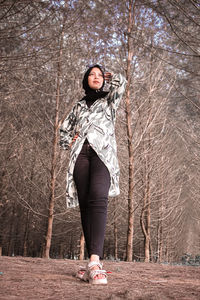 Portrait of woman standing by bare tree in forest