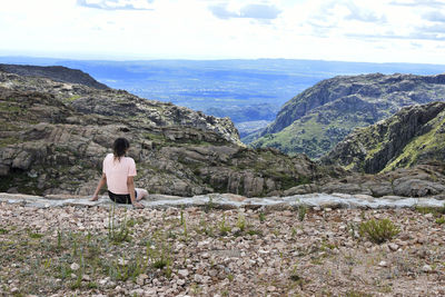 Rear view of woman sitting on rock against mountains