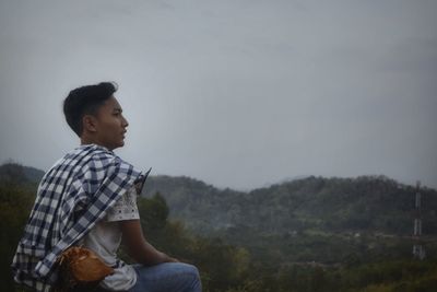 Side view of young man looking away by mountain against sky