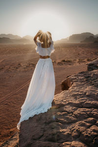 Rear view of woman standing on sand at beach against clear sky