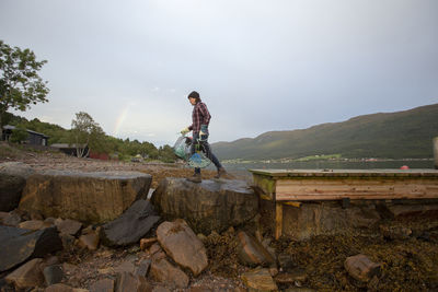 A fisherman walking along some rocks at a fjord in norway