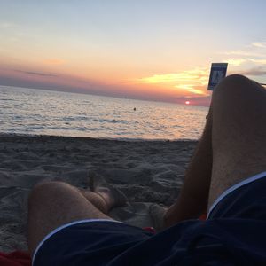 Low section of people sitting on beach at sunset