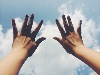 Low angle view of cropped hand against cloudy sky