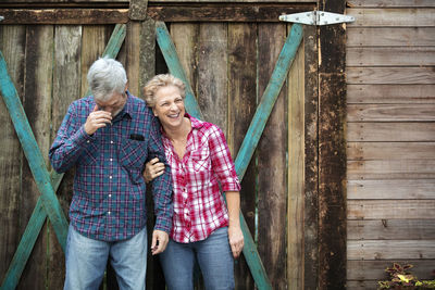 Happy senior couple standing against log cabin in forest