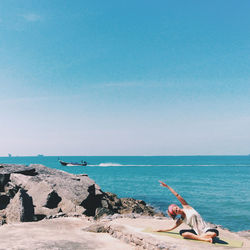 Young woman practicing yoga while sitting on rock formation at beach