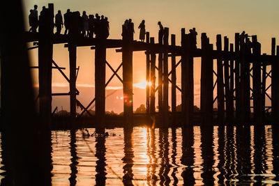 Silhouette people on pier over lake against sky during sunset