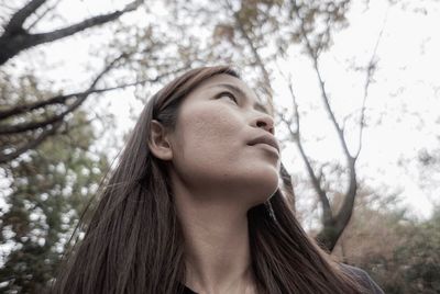 Low angle view of young woman looking up against tree