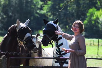 Blonde woman feeding a horse among tall trees in summer,countryside, rural