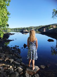 Rear view of girl standing on rock while looking at lake