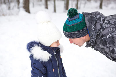 Dad and daughter look at each other closely in warm clothes, hats with a pompom on the stree