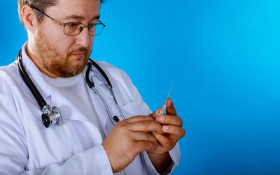 Doctor holding syringe against blue background