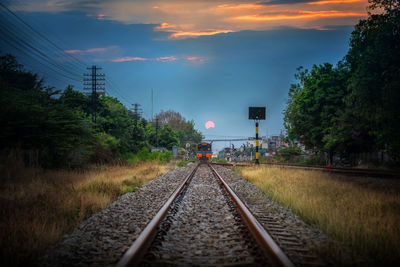 Railroad track amidst trees against sky during sunset