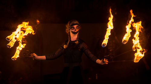 Woman holding sticks with flame while standing at night during event