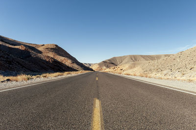 Road leading towards mountains against clear sky