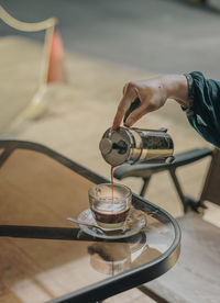 Cropped hand pouring coffee in cup at table