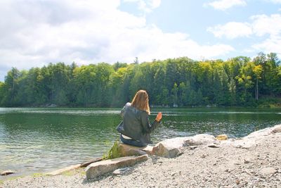 Woman sitting by lake against sky